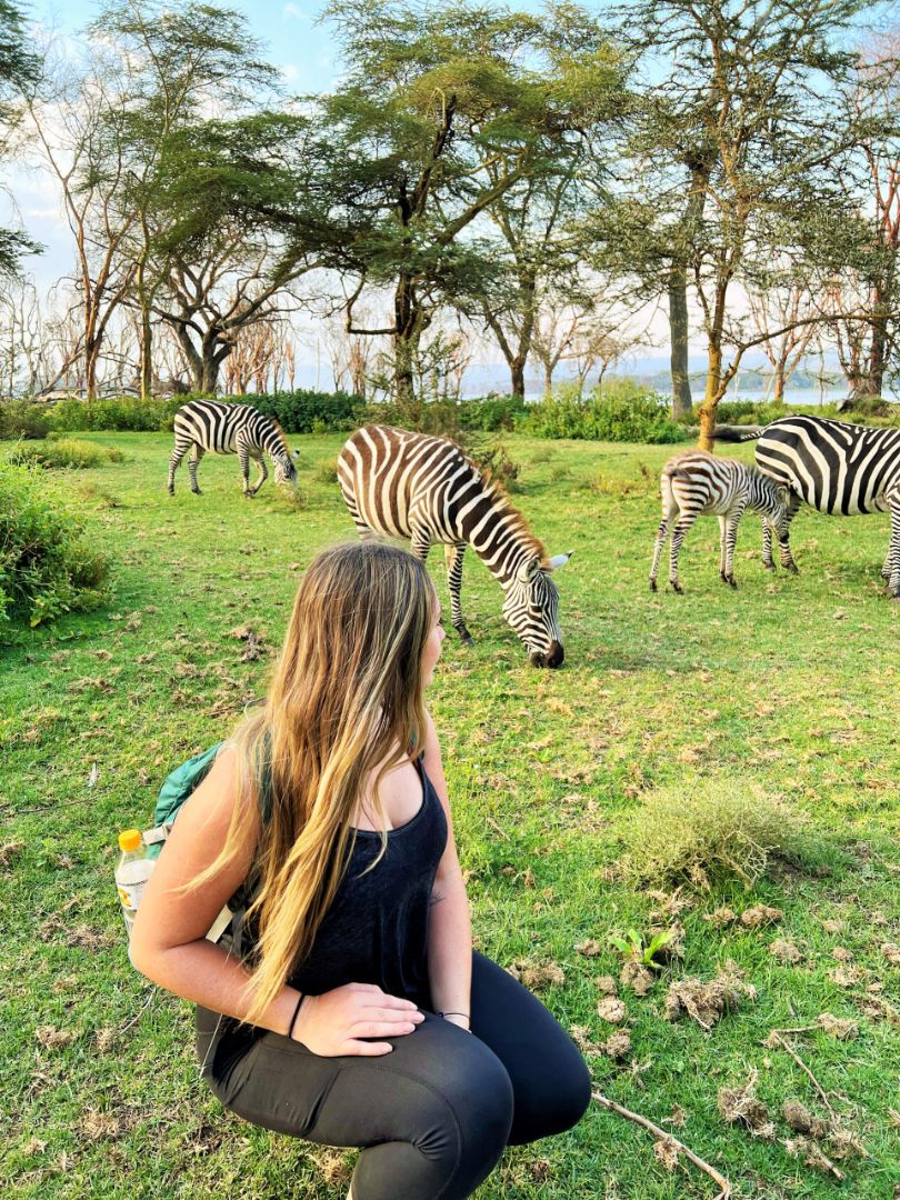 A traveller enjoying a moment beside grazing zebras in Kenya